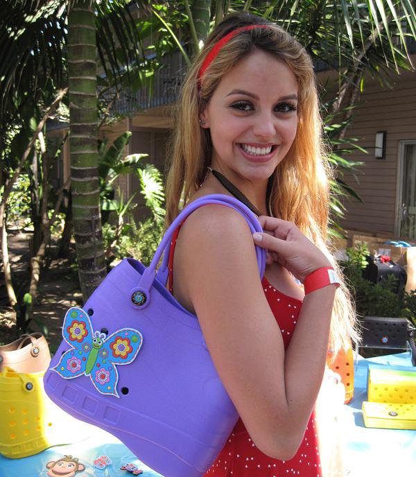 Woman dressed in red holds a purple Crocs-inspired bag over her shoulder, with a butterfly clip attached to it